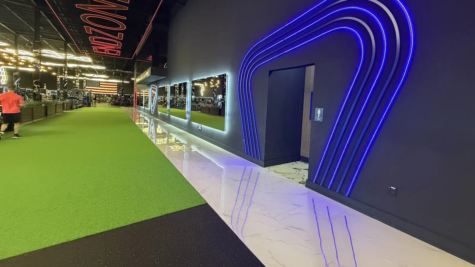 Acceleration vs max velocity training: the indoor turf sprint lane at 1st & Goal Athletics in Ocean Township, NJ, running past the lit arch toward the weight floor