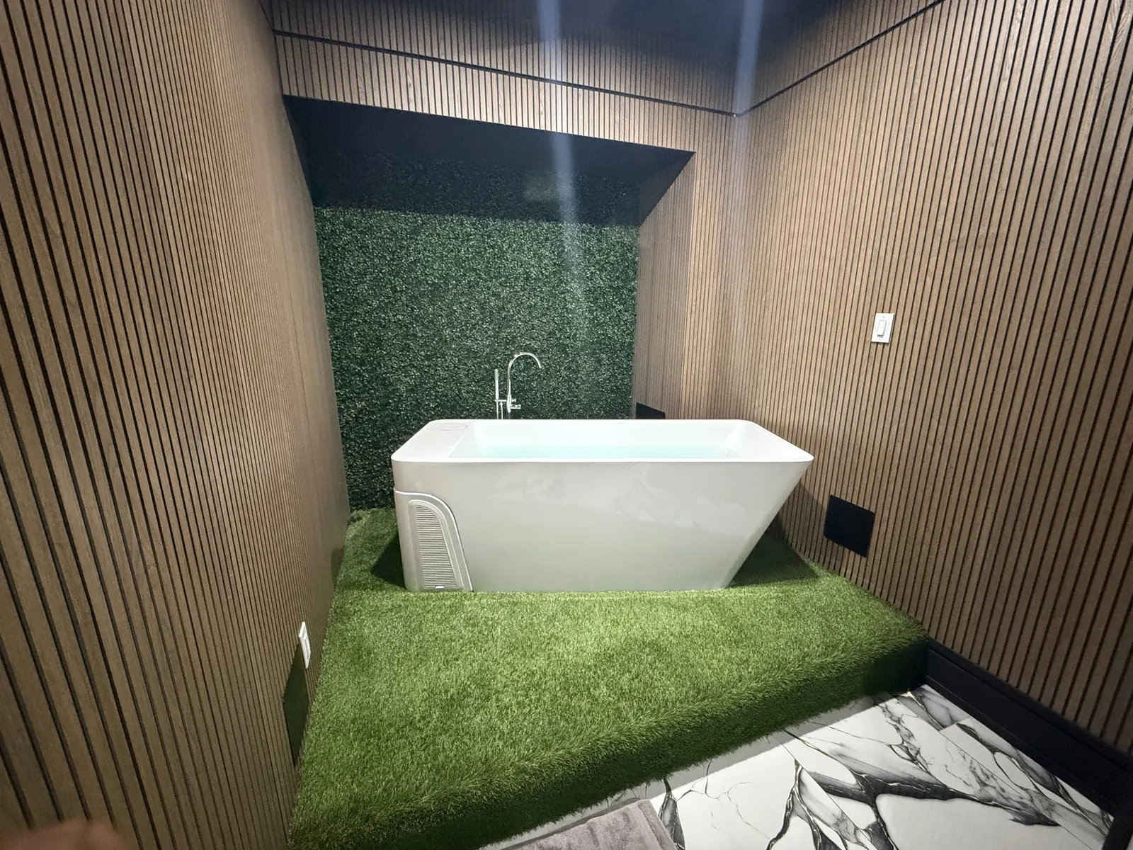 White cold plunge tub set on turf against a greenery wall