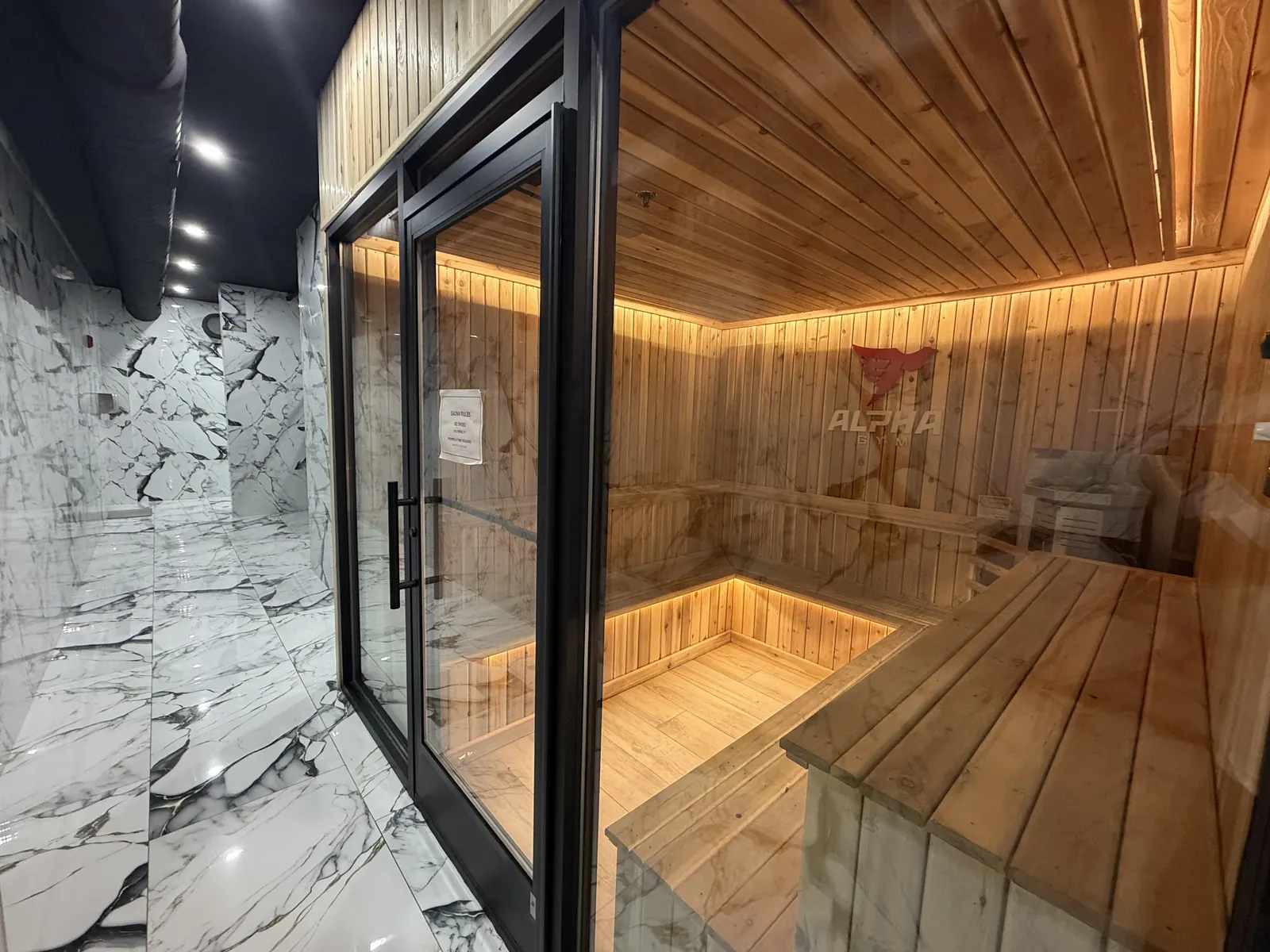 Cedar sauna behind a glass door with a marble-tiled entry