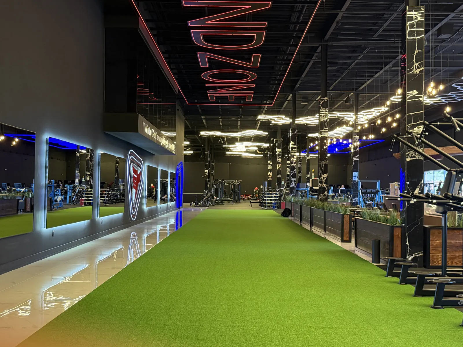Indoor turf lane under a red ENDZONE sign, mirrors along the left wall, the weight floor beyond