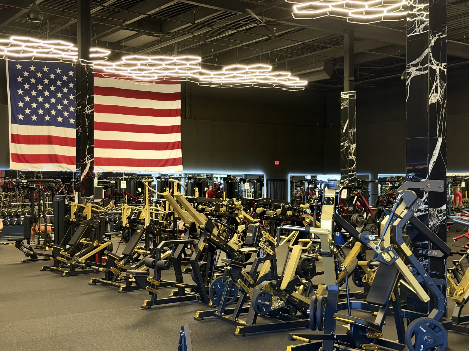 Weight floor with plate-loaded machines under hex lights and an American flag